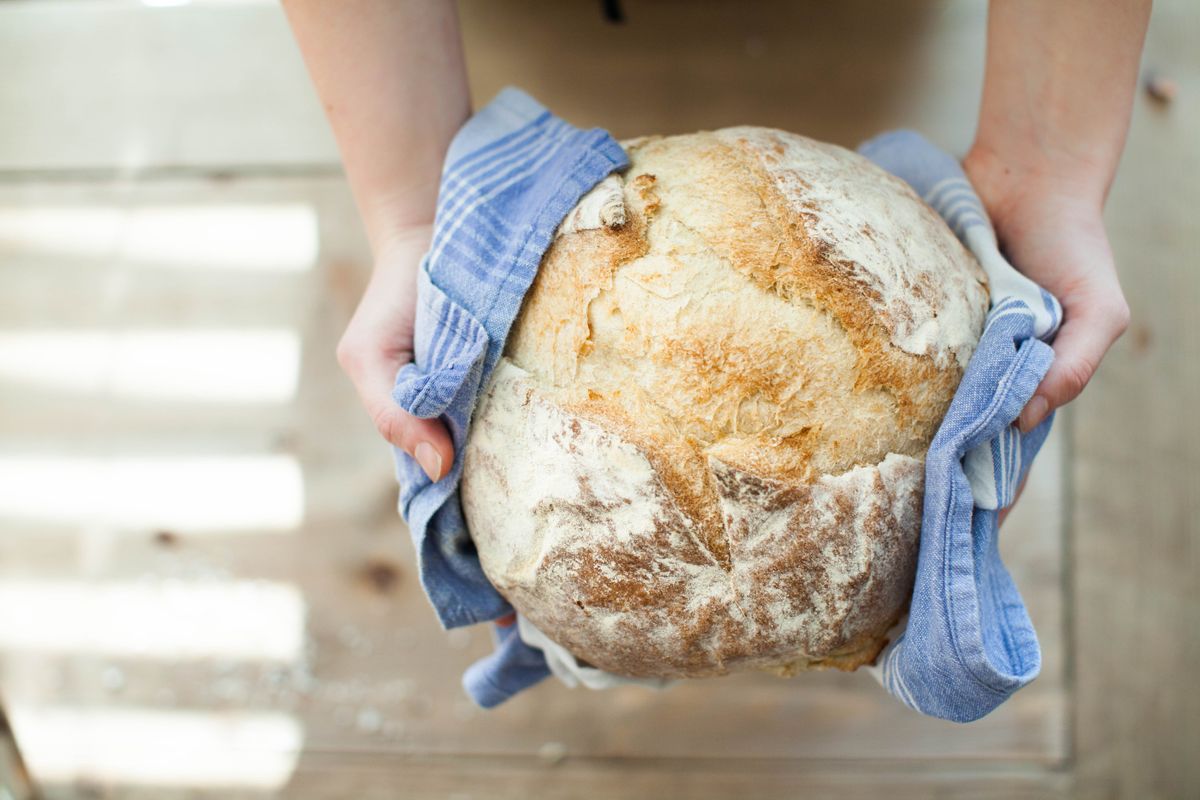 Hands holding a round artisan loaf wrapped in a striped cloth
