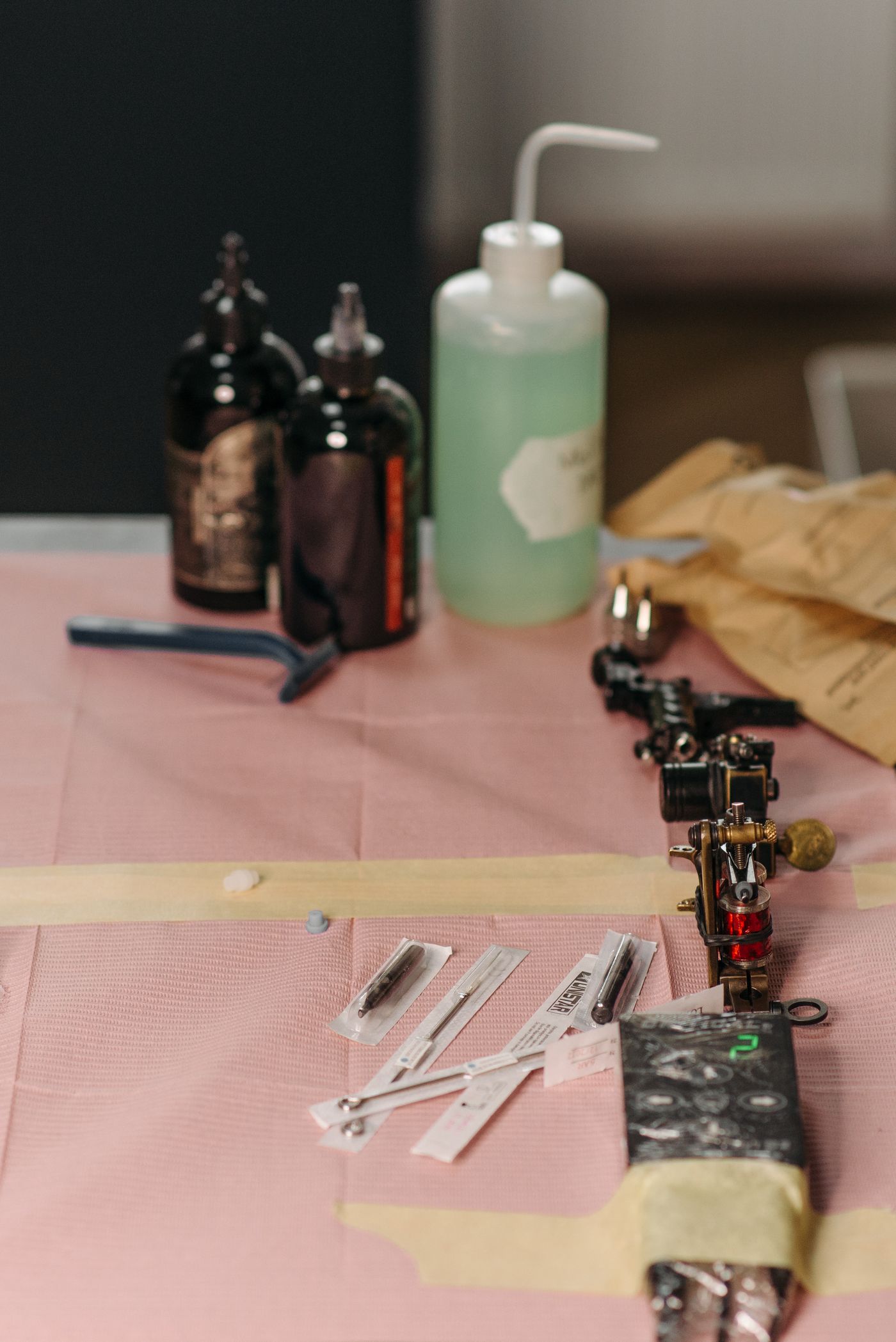 A tattoo machine, wrapped needles and bottles laid out on a covered workstation