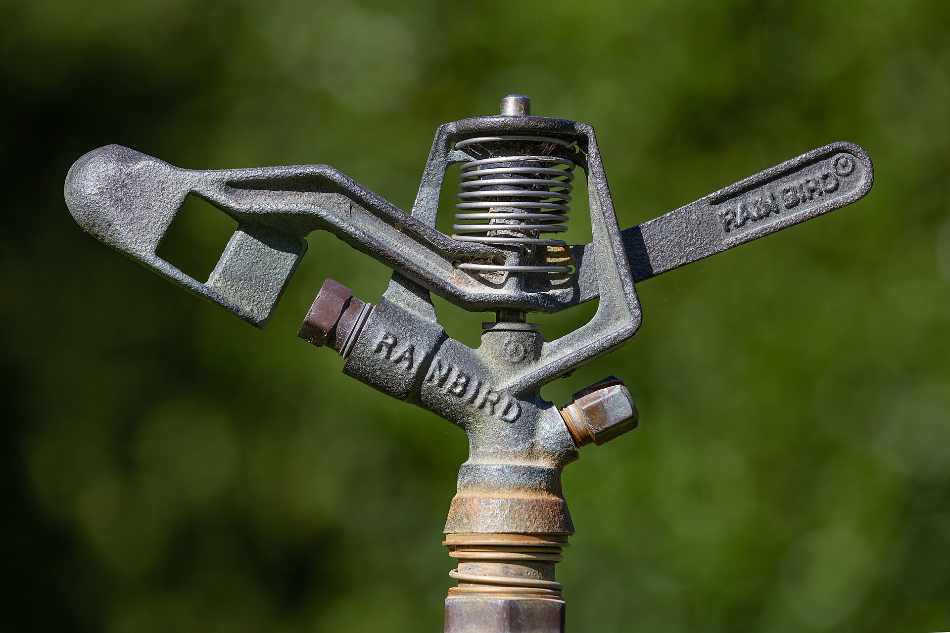 A close-up of an impact sprinkler head against a green lawn