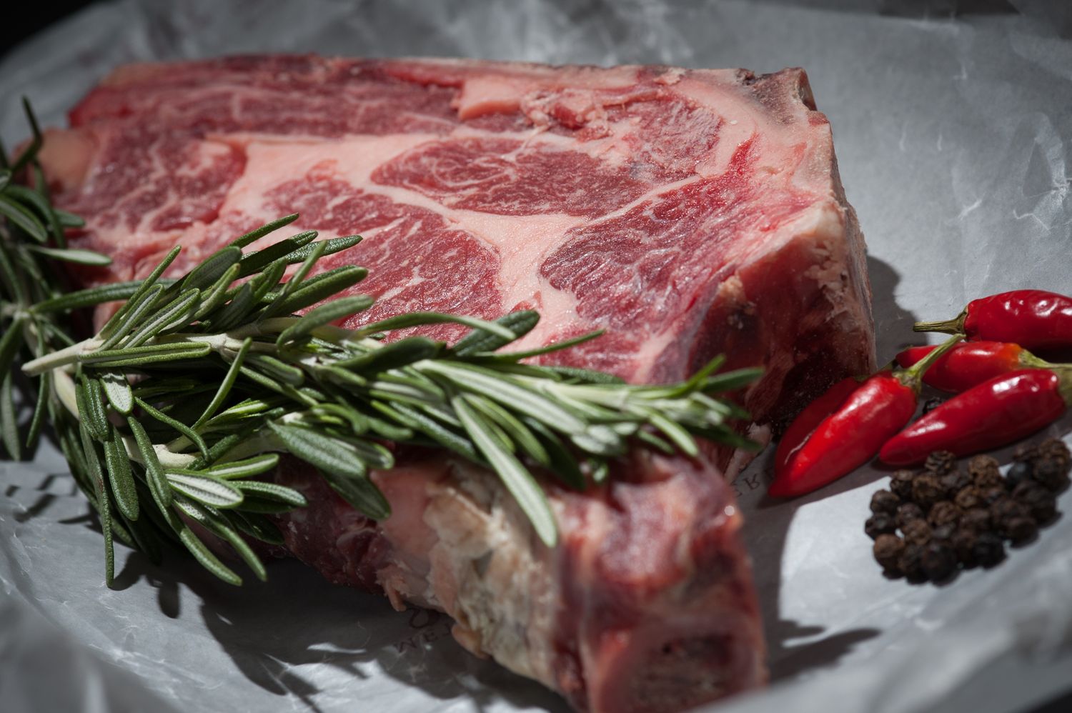 A raw ribeye with rosemary and chilli on a butcher's board