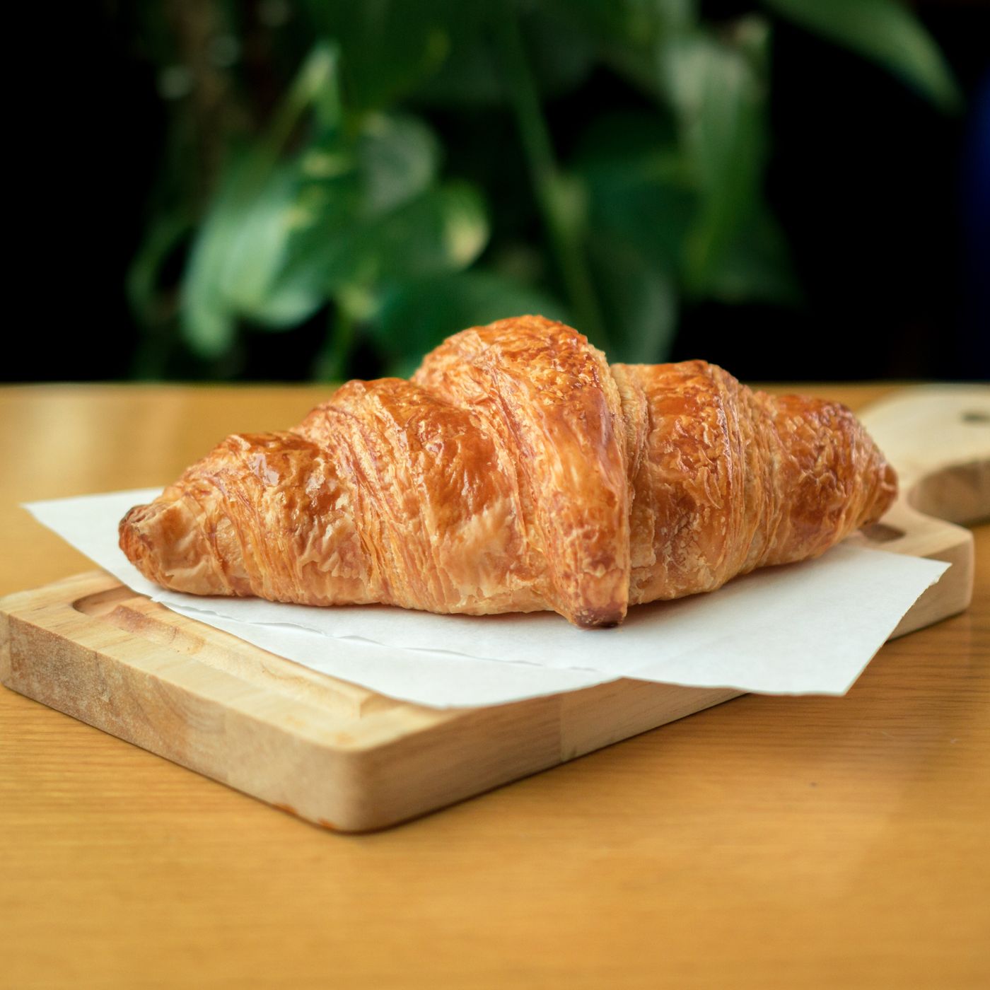 A flaky golden croissant on a wooden board
