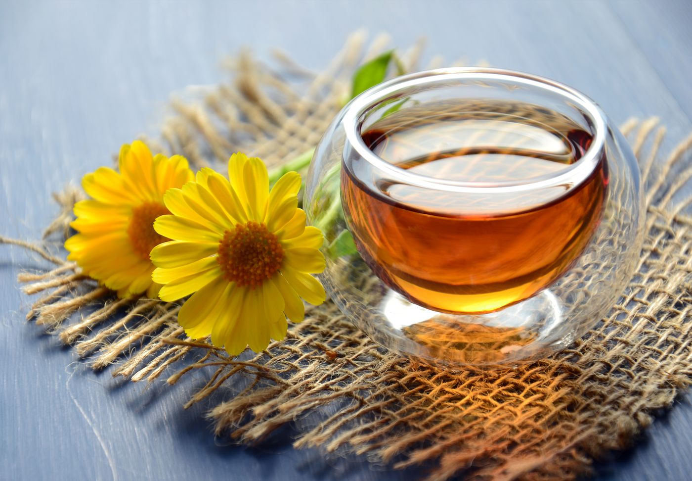Amber honey-coloured tea in a glass beside a golden flower, warm still life