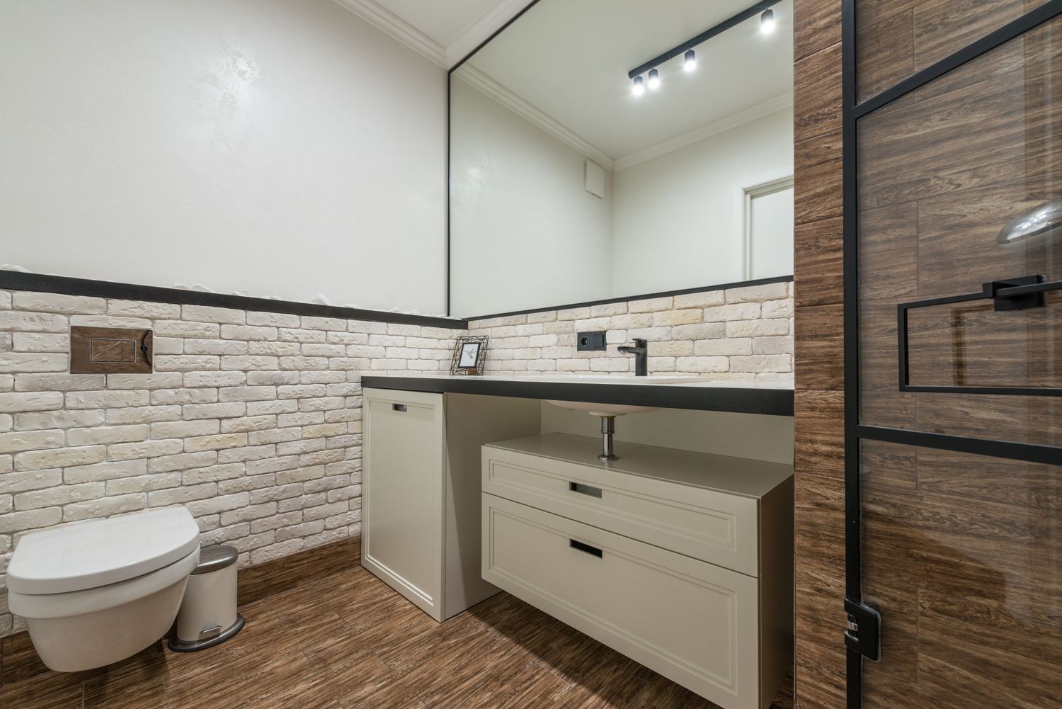 A renovated powder room with brick-style tile wall, vanity and wood-look tile