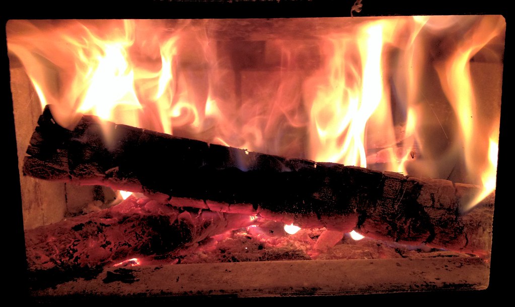 A glowing log fire behind the glass of a stove